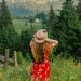 woman in red and white floral dress wearing brown sun hat standing on green grass field